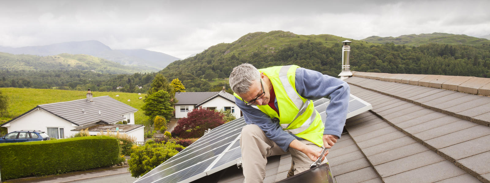 A workman fitting solar thermal panels for heating water, to a house roof in Ambleside, Cumbria, UK, that already has solar PV for generating electricity.