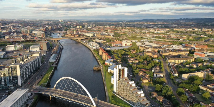 Aerial view of city of Glasgow showing buildings, a river, a bridge over the river, houses, and trees.