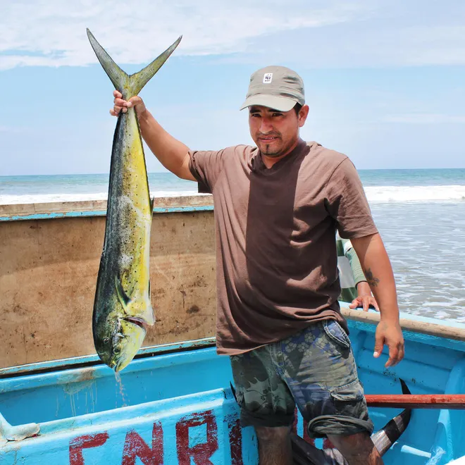A man standing in a boat holds a large fish that he caught