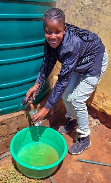 Nkarabeleng Matabane stands next to her rainwater collection tank
