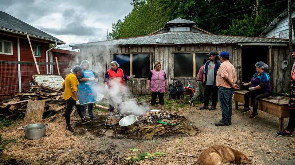 Women cook around a fire with the backdrop of their village