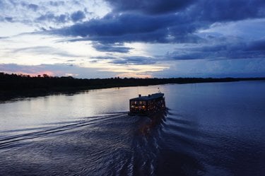 A riverboat moving along the river at night at night with its lights reflecting off the water