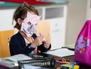 A photo of a young student at a school desk wearing a crafted tiger mask.