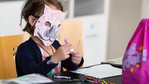 A photo of a young student at a school desk wearing a crafted tiger mask.