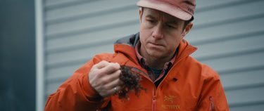 A man in an orange jacket holds up seaweed.