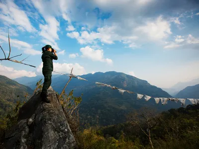 Ranger Singye Wangmo stands on a rock looking through binoculars