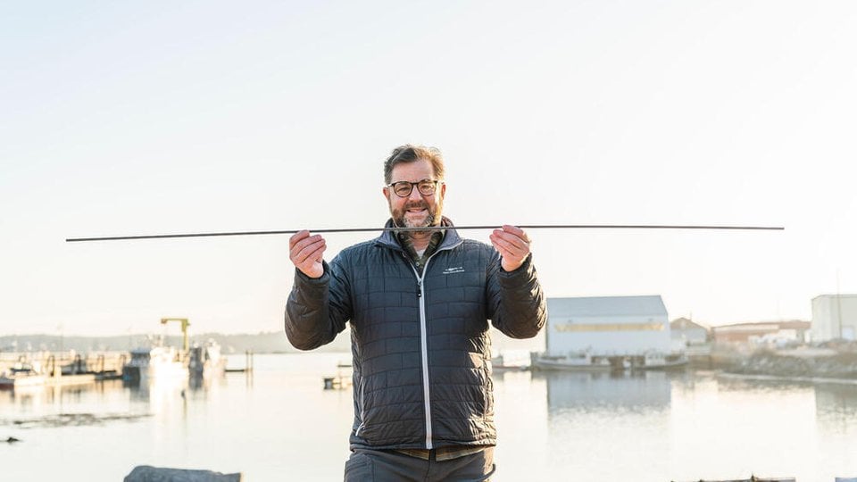 A man standing in front of a waterway holding a long stick.