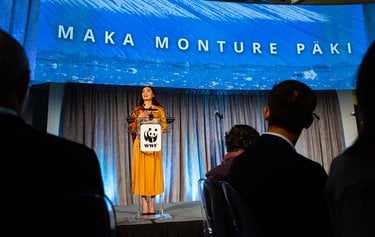 Maka Monture Päki stands behind a WWF podium with hands over her heart while making a stage making a speech.