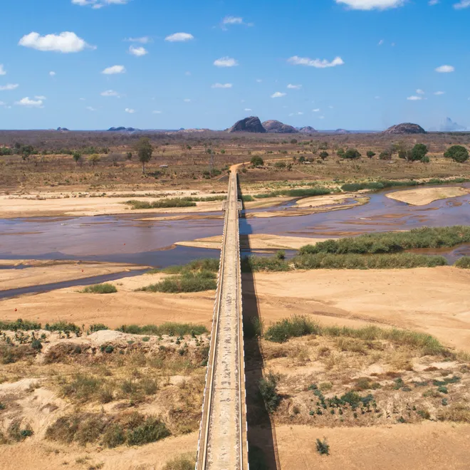 Aerial photo of a bridge over a river that connects to a dirt road in a desert landscape