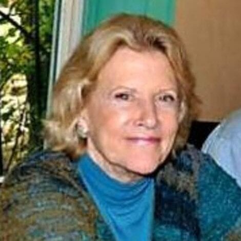 A woman with blonde hair and a bright turquoise shirt and multicolored sweater.