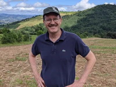 A white man stands in front of green rolling hills