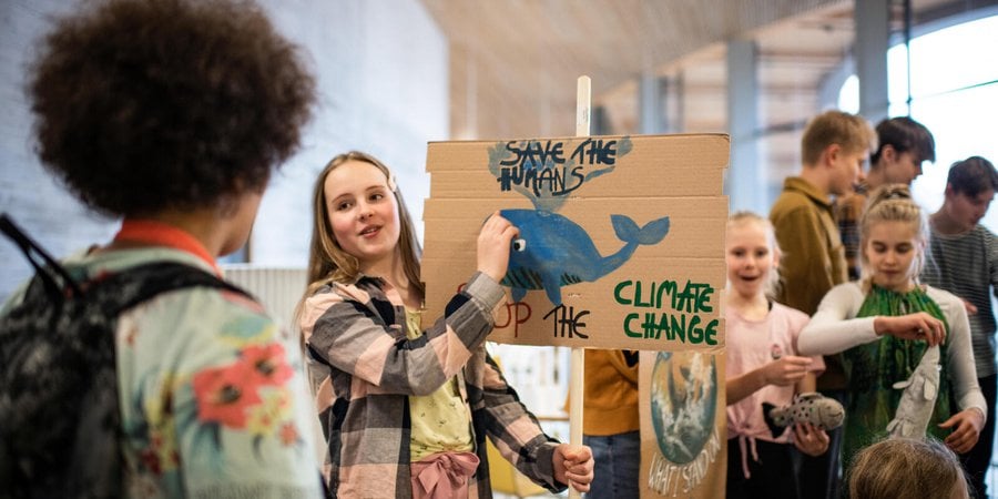 A young girl holds up a cardboard sign with a whale that says "Save the humans" and "Stop the climate change"