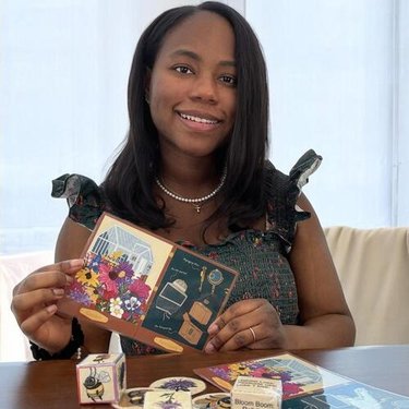 A woman with dark hair sits at a table holding up a card.