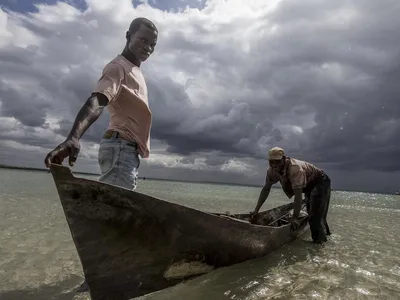 Two men in a canoe at the edge of a waterway with dark clouds in the background.