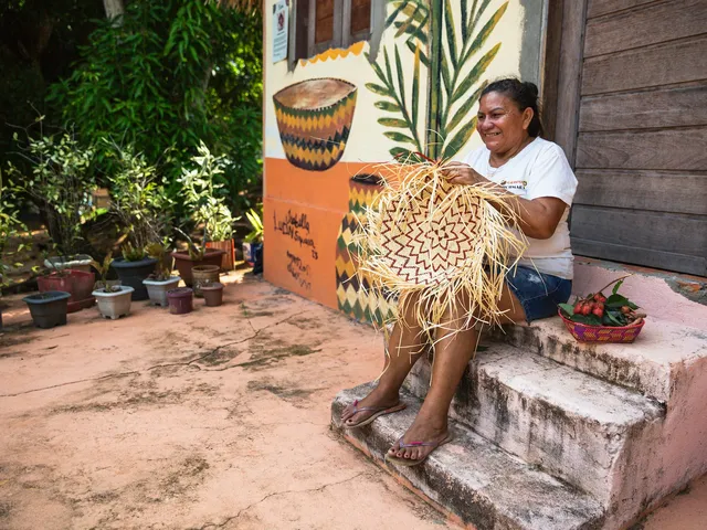 An Indigenous woman makes basket crafts on the steps in front of her house in the Urucurea community in Brazil.