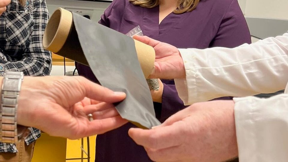 Three people holding up a piece of fabric in a laboratory.
