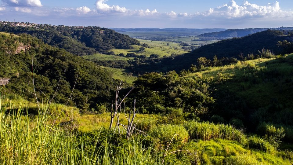 A landscape view of a lush, green valley in Brazil with clouds and blue sky