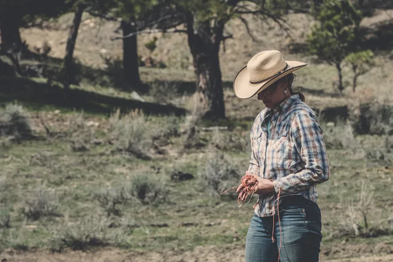 Rancher Heather Bilden wears a cowboy hat and looks down at her hands on her ranch