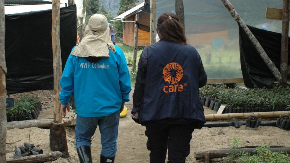 Two people walk away from camera, one in a WWF-Colombia jacket, the other in a CARE jacket