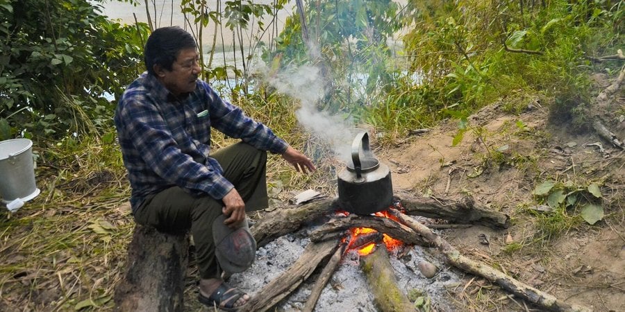 A man sits at a campfire in the woods cooking something over the flames