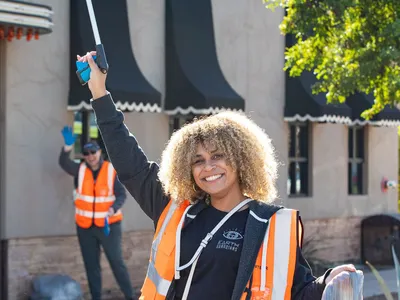 Emmy Scott holds a trashbag and raises a garbage picker in the air at a community cleanup