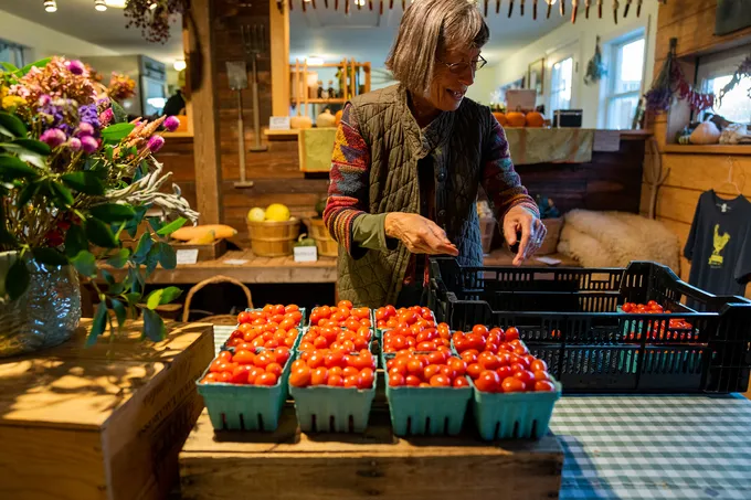 Woman stands in front of row of grape tomatoes at market