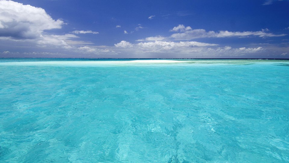 A clear, light sky blue ocean with a blue sky and a few clouds