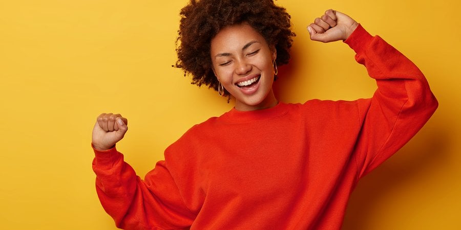 Woman celebrates with her eyes closed and her hands up against a solid background