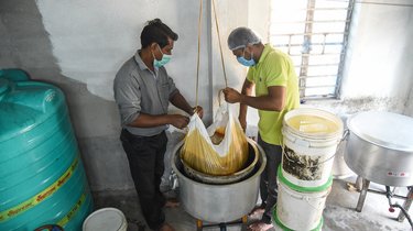 Two men hold filter over pot