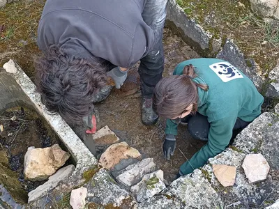 Two people working in a stone-lined hole