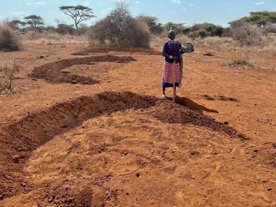 A female farmer stands next to half-moon shaped areas of fertile soil