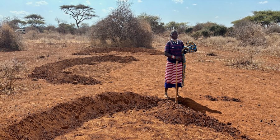 A female farmer stands next to half-moon shaped areas of fertile soil