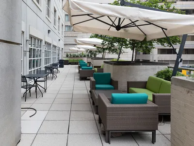 A building patio with cement tile, gray chairs with teal pillows, and large white umbrellas