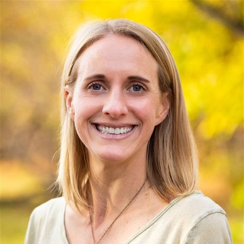 Leigh Prezkop wears a beige shirt and smiles in front of a yellow background