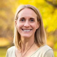 Leigh Prezkop wears a beige shirt and smiles in front of a yellow background
