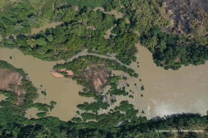 An aerial view of the Srepok River shows brown water flowing for forested and rocky areas