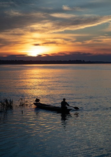 A person in a canoe watches a brilliant sunrise or sunset on the Amazon River.