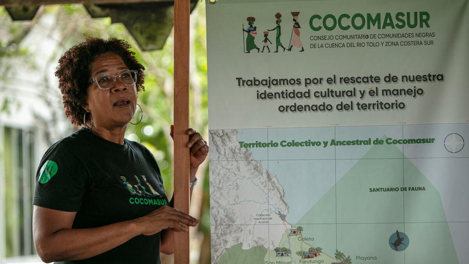 Everildys Cordoba, Cocomasur community council leader in Acandí, Chocó, Colombia, wears a green shirt and stands in front of a large map.
