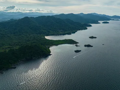 An aerial view of Acandí, Playón and Playona Wildlife Sanctuary, showing glimmering blue water and forest-covered mountains