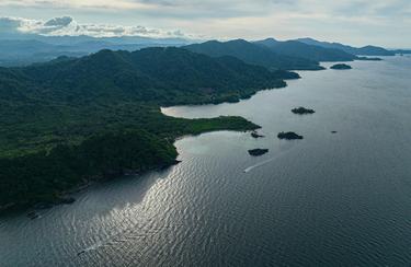 An aerial view of Acandí, Playón and Playona Wildlife Sanctuary, showing glimmering blue water and forest-covered mountains