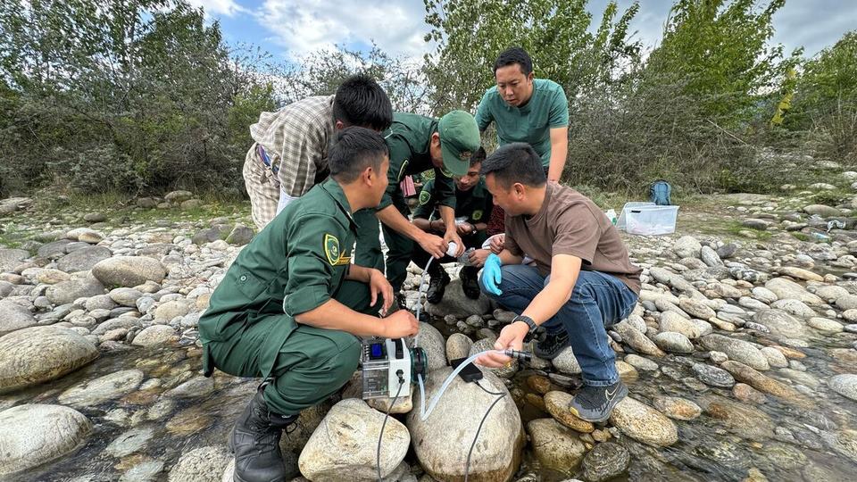 Several men standing over scientific equipment on a rocky riverside