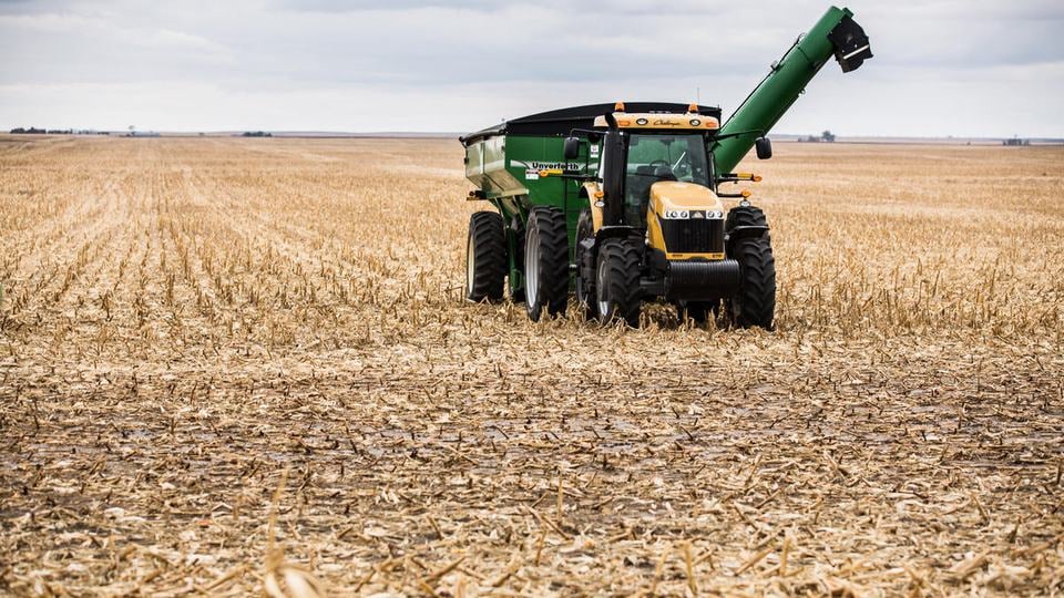 A tractor and harvester sit in a cleared cornfield