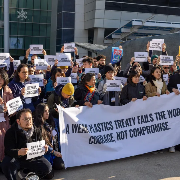 A group of people stand in front of a banner reading "A weak plastics treaty fails the world. Courage, not compromise."