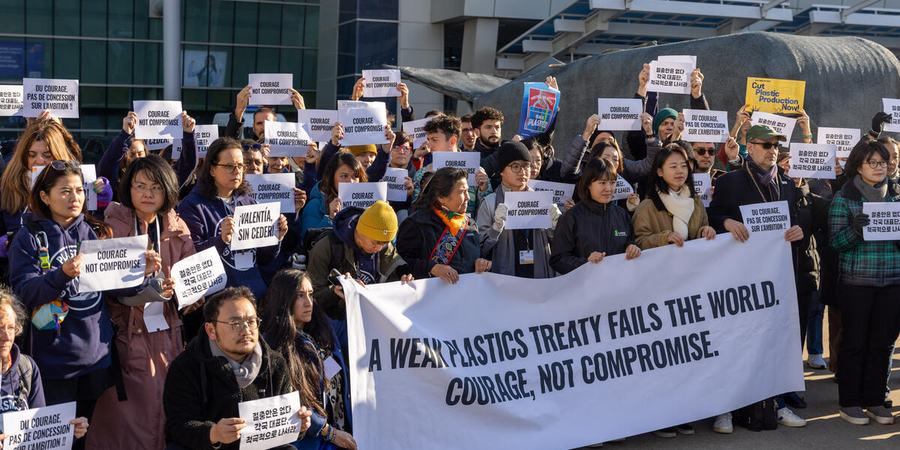 A group of people stand in front of a banner reading "A weak plastics treaty fails the world. Courage, not compromise."