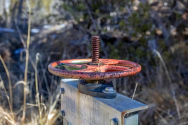 An irrigation valve with a red, circular mechanism attached to a metal box sits among grasses