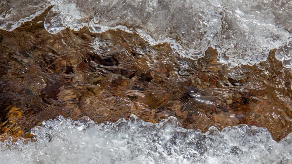 A close up of rushing white water over reddish-brown stone in the Rio Quemado