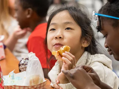 Students Students Alice T. and Kyla P. eat lunch in the cafeteria at Citrus Elementary School, holding an orange and sitting at a table