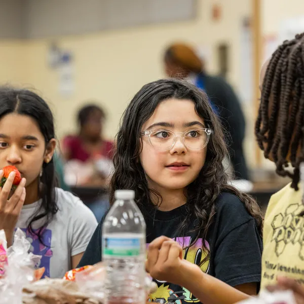 Maria S. and Isabella I., two students with dark hair, one with glasses, sit at a cafeteria table wiht their lunches in front of them