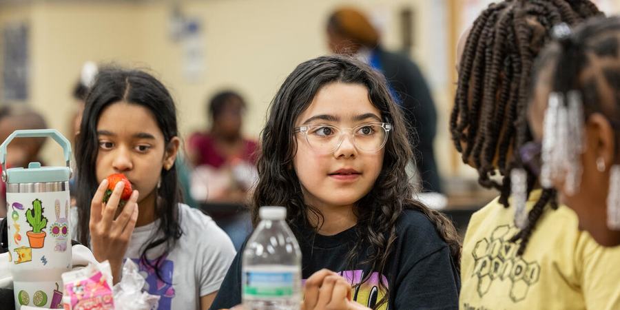 Maria S. and Isabella I., two students with dark hair, one with glasses, sit at a cafeteria table wiht their lunches in front of them