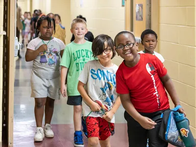 Smiling students in red, white, green shirts line up as a group to go to lunch